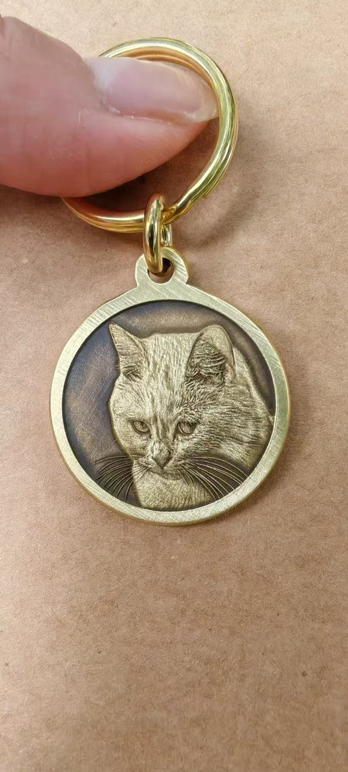 Close-up of a round gold-tone custom pet portrait pendant held between two fingers